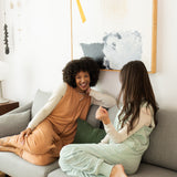 2 women sitting on a couch wearing comfortable bamboo adult sleep sacks 