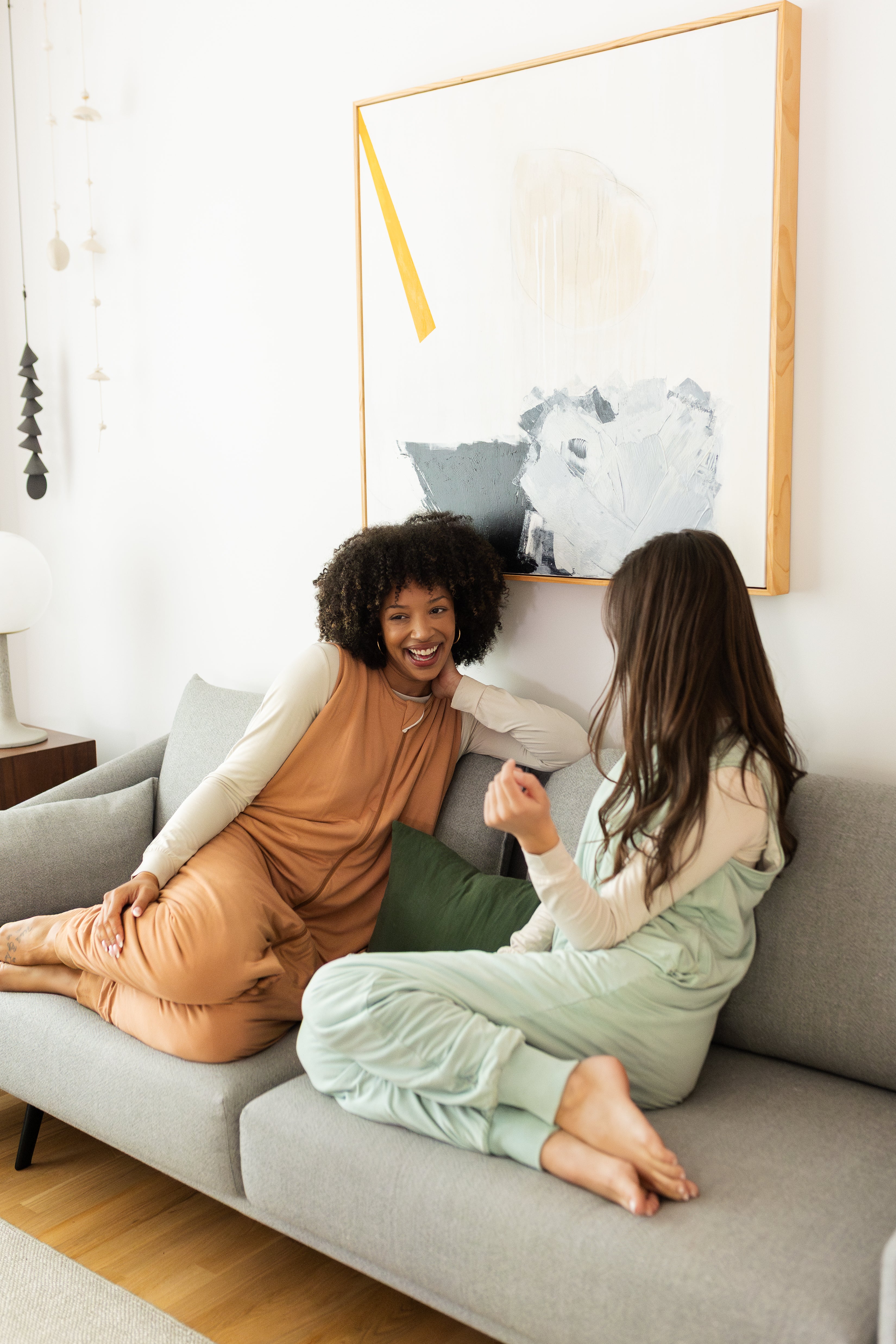 2 women sitting on a couch wearing comfortable bamboo adult sleep sacks 