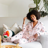 Woman smiling in pink sushi pajamas sitting on a white couch with a plant in the background
