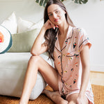 Model wearing Pink Women's Short Sleeve Pajama Set in Sushi print sitting beside a white couch in a living room. ::: Model is 5'10" wearing size S ///
---PJ 4