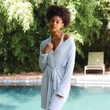 Woman in a light blue robe standing by a pool with greenery in the background