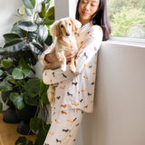 Model wearing Long-Sleeved Women's Pajama Set in Dachshund standing against a wall near a tree holding a Dachshund dog
::: Model is 5'6" wearing size XS ///