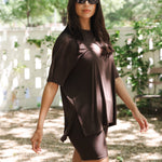 Woman wearing a brown dress and sunglasses outdoors with greenery in the background