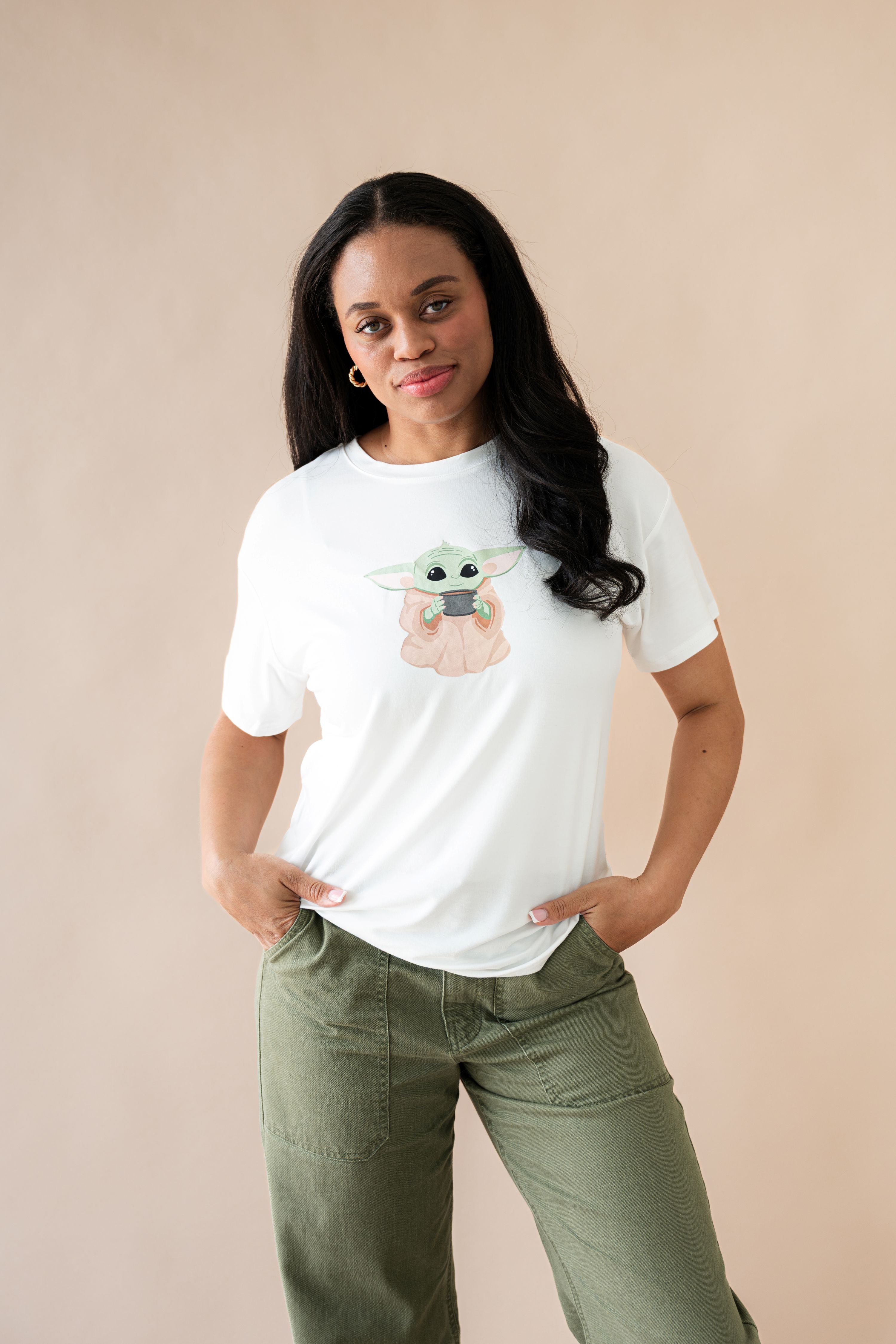 Female posing wearing the Women's Graphic Tee in The Child™ paired with dark green pants

