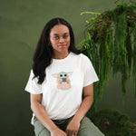 Female sitting on a tree stump with greenery on it wearing the Women's Graphic Tee in The Child™