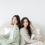 Models sitting on a bed back to back while wearing the Long-Sleeved Women's Pajama Set in Starry Icon and Honey Dukes 