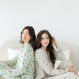 Models sitting on a bed back to back while wearing the Long-Sleeved Women's Pajama Set in Starry Icon and Honey Dukes 