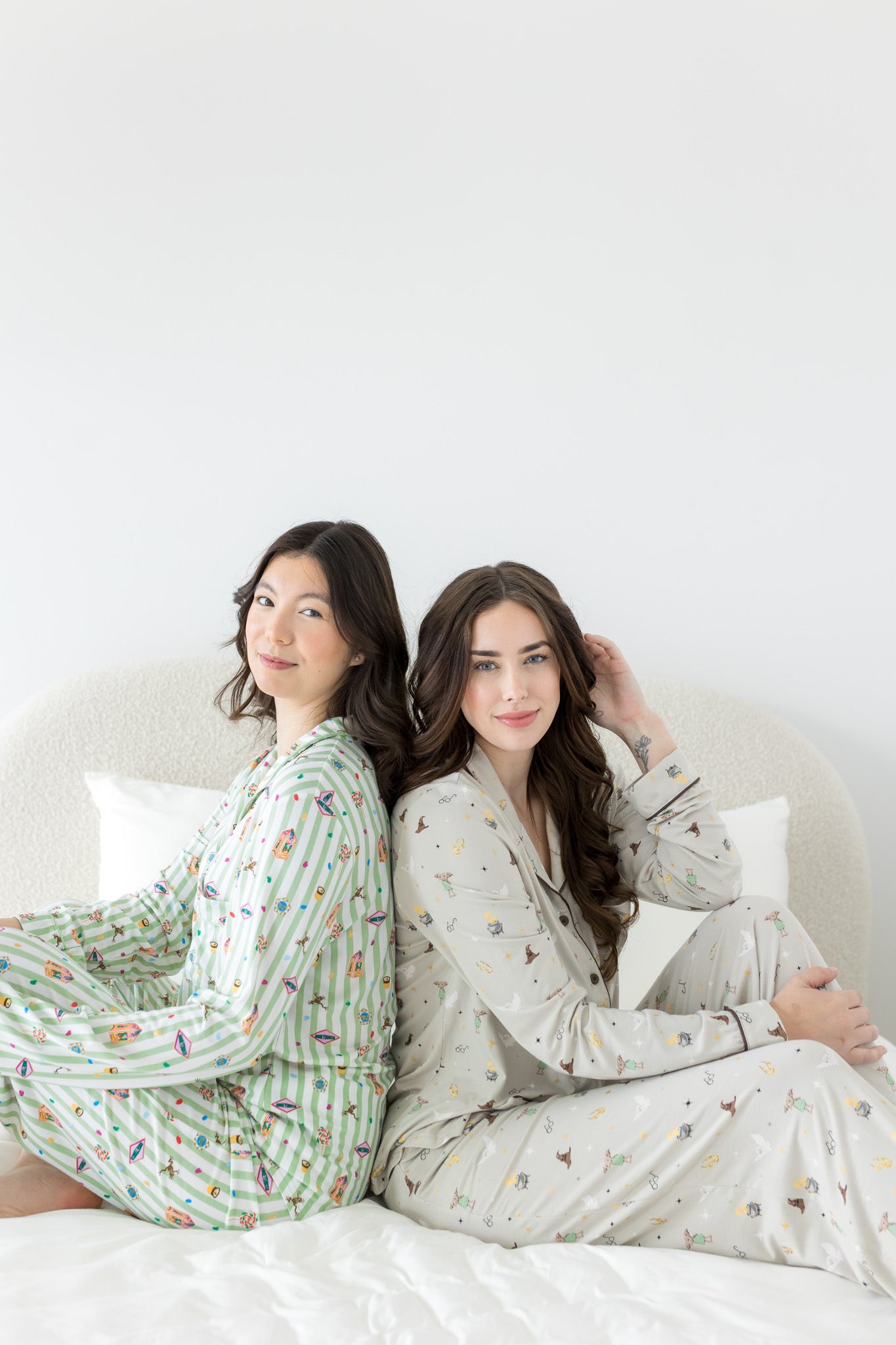 Models sitting on a bed back to back while wearing the Long-Sleeved Women's Pajama Set in Starry Icon and Honey Dukes 