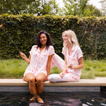 Two Models sitting by the pool side enjoying in Women's Short Sleeve Pajama Set and Women's Short Sleeve Cropped Pajama Set in Sakura Ice Cream print