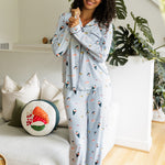 Woman wearing a light blue pajama set with colorful sushi patterns standing in a cozy living room. ::: Model is 5'10" wearing size S ///
