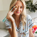 Woman holding a sushi in chopsticks wearing blue Short sleeve women's pajamas set in sushi print sitting on a white couch