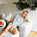 Woman sitting on a white couch in a home setting with plants wearing a blue Women's Short Sleeve Pajama Set in Sushi print ---1615 3