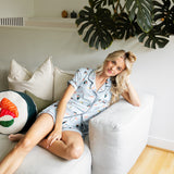 Woman sitting on a white couch in a home setting with plants wearing a blue Women's Short Sleeve Pajama Set in Sushi print ---1615 3