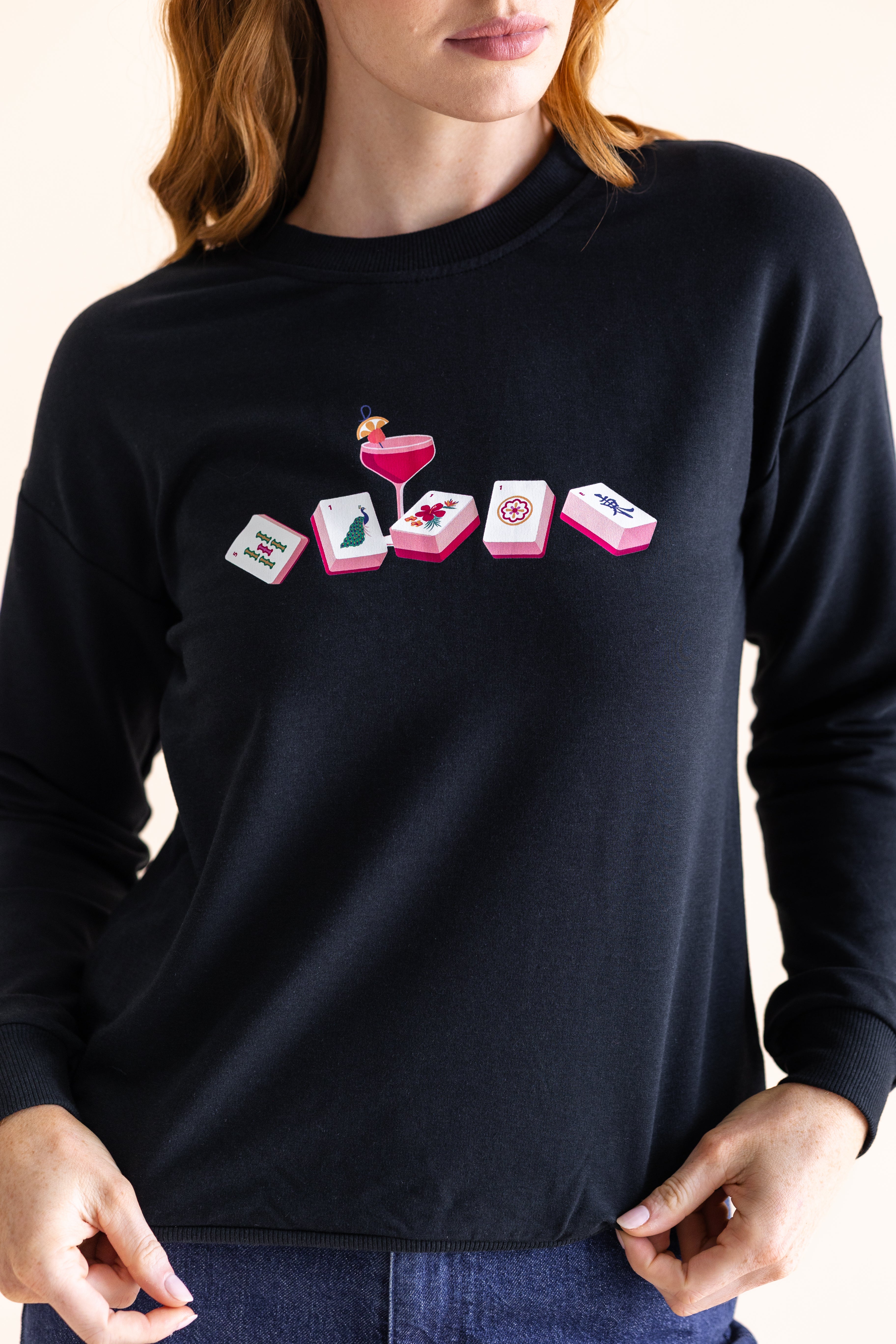 Person wearing a black long-sleeve sweatshirt with a mahjong graphic design on a plain background