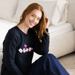 Woman wearing a black sweatshirt with colorful mahjong graphics sitting next to a bed.