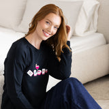 Woman wearing a black sweatshirt with colorful mahjong graphics sitting next to a bed.