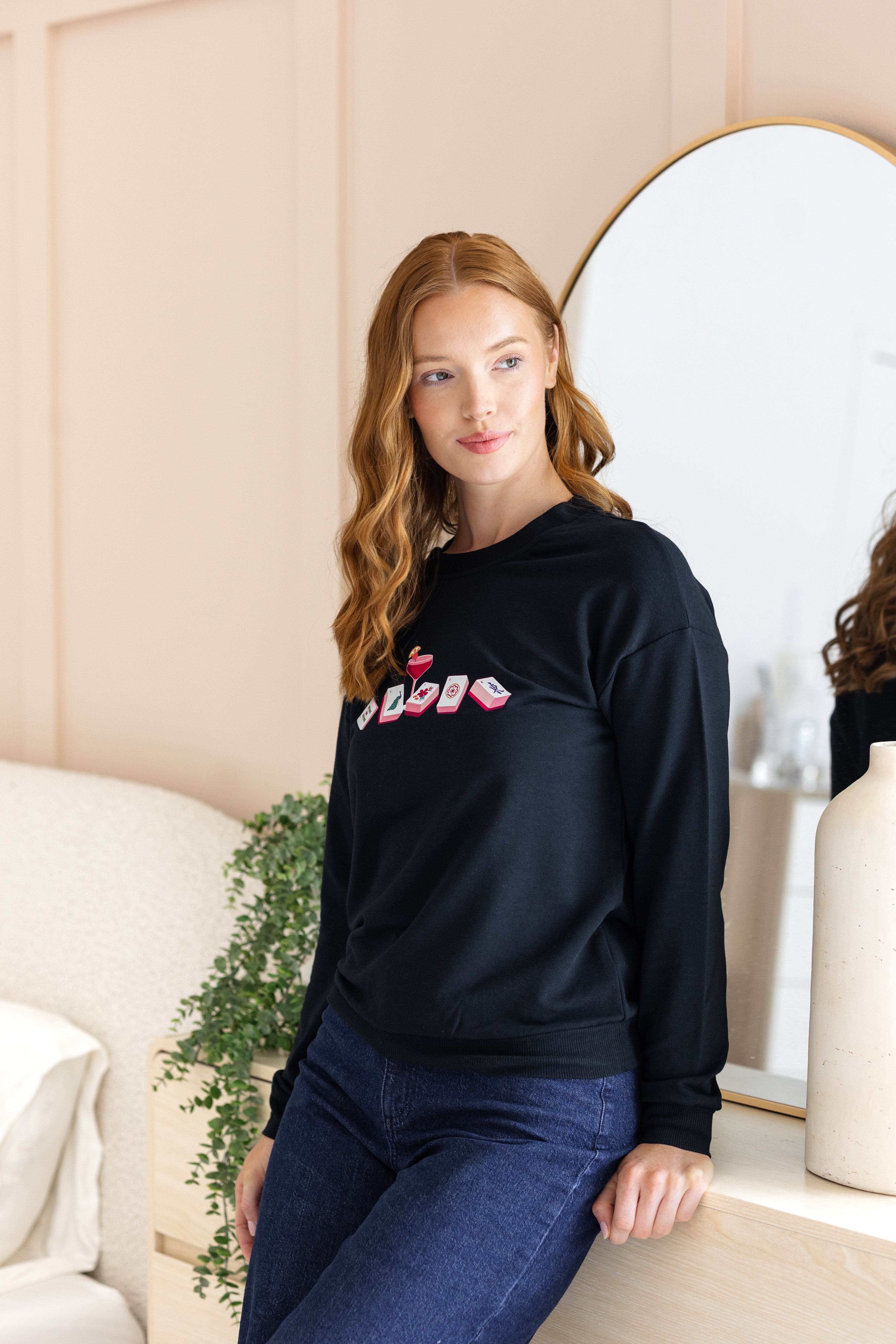 Woman wearing a black sweatshirt with colorful mahjong design in a room.
