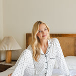 Woman in polka dot pajamas sitting on a bed in a bedroom.
---1605 3