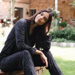 Woman in black leopard outfit sitting on a wooden stump outdoors  