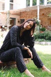 Woman in black leopard outfit sitting on a wooden stump outdoors  
