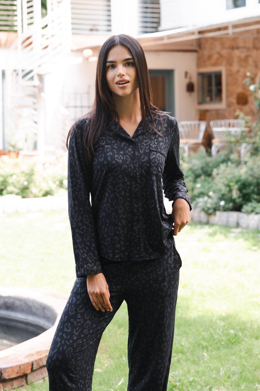 Woman wearing a black leopard patterned outfit standing outdoors in a garden.