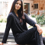 Woman in a black leopard pajama set sitting outdoors on a stone ledge.