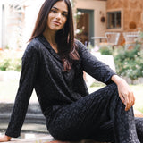 Woman in a black leopard pajama set sitting outdoors on a stone ledge.