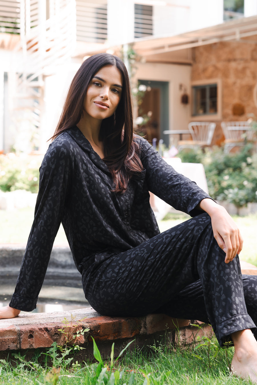Woman in a black leopard pajama set sitting outdoors on a stone ledge.