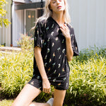 Model posing outdoors in sunlight wearing Women’s Biker Short Set in Midnight Wildflower print with bushes in the background