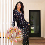 Model wearing Long-Sleeved Women's Pajama Set in Midnight Wildflower print standing outdoors holding a flower wreath ::: Model is 5'10" wearing size S /// ---PJ 2
