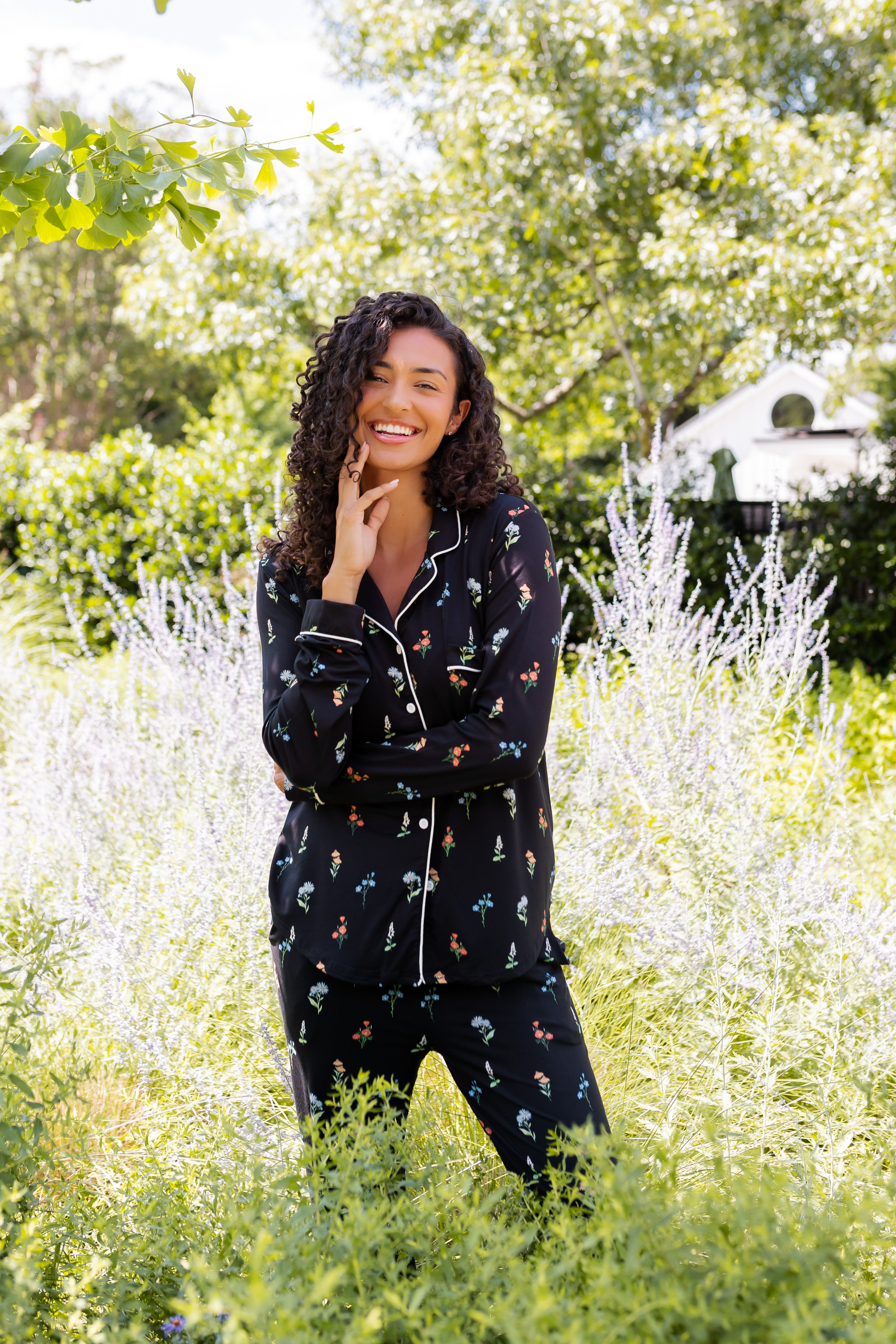 Model smiling outdoors between bushes in Long-Sleeved Women's Pajama Set in Midnight Wildflower print