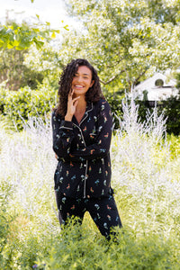 Model smiling outdoors between bushes in Long-Sleeved Women's Pajama Set in Midnight Wildflower print