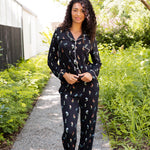 Model wearing Long-Sleeved Women's Pajama Set in Midnight Wildflower print standing outdoors surrounded by trees ---1605 1