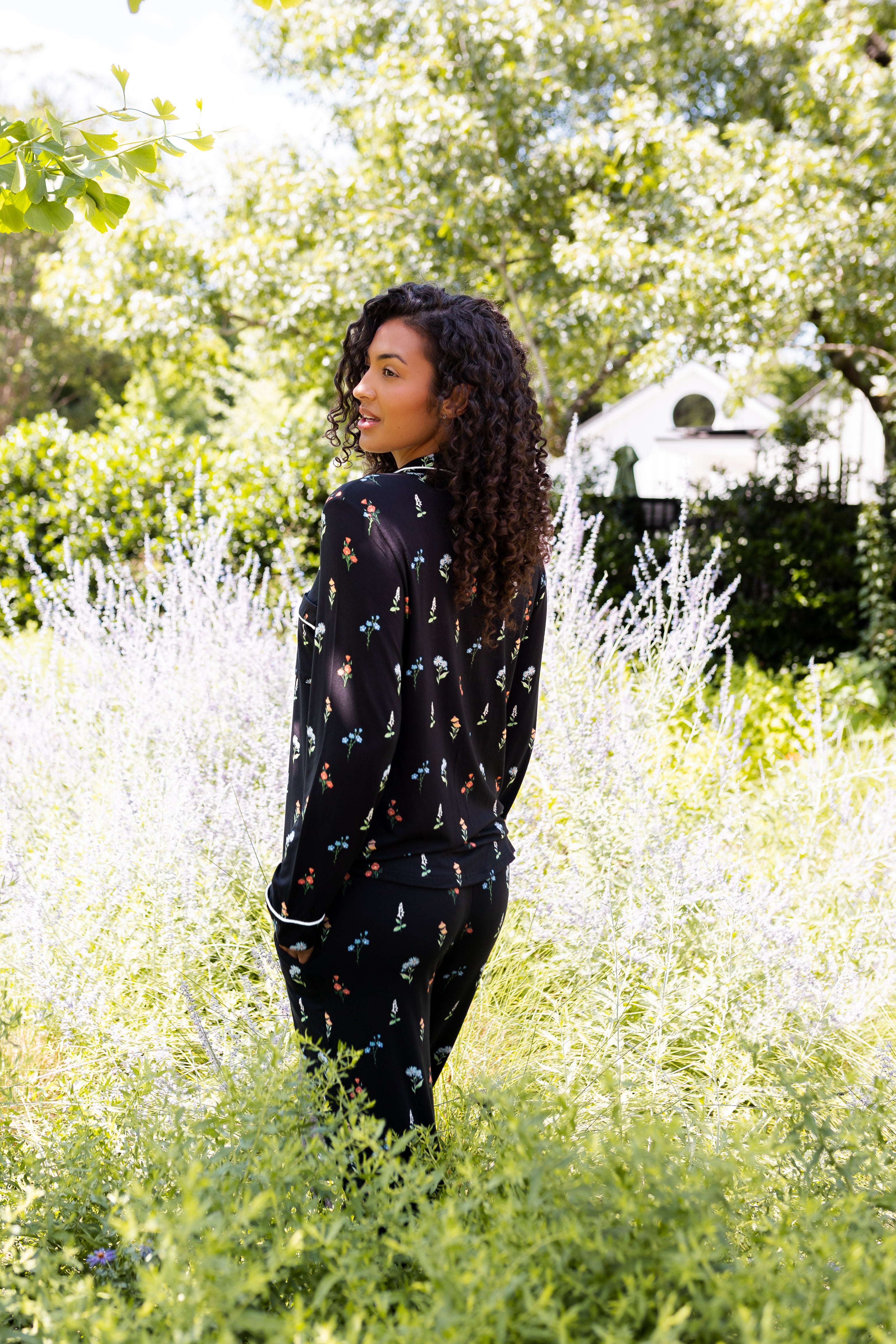Model posing outdoors in bushes back side of Long-Sleeved Women's Pajama Set in Midnight Wildflower print