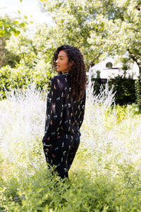 Model posing outdoors in bushes back side of Long-Sleeved Women's Pajama Set in Midnight Wildflower print