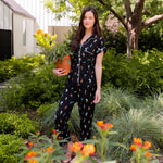 Model standing outdoors surrounded by trees holding a pot wearing Women's Short Sleeve Cropped Pajama Set in Midnight Wildflower  ::: Model is 5'10" wearing size S ///