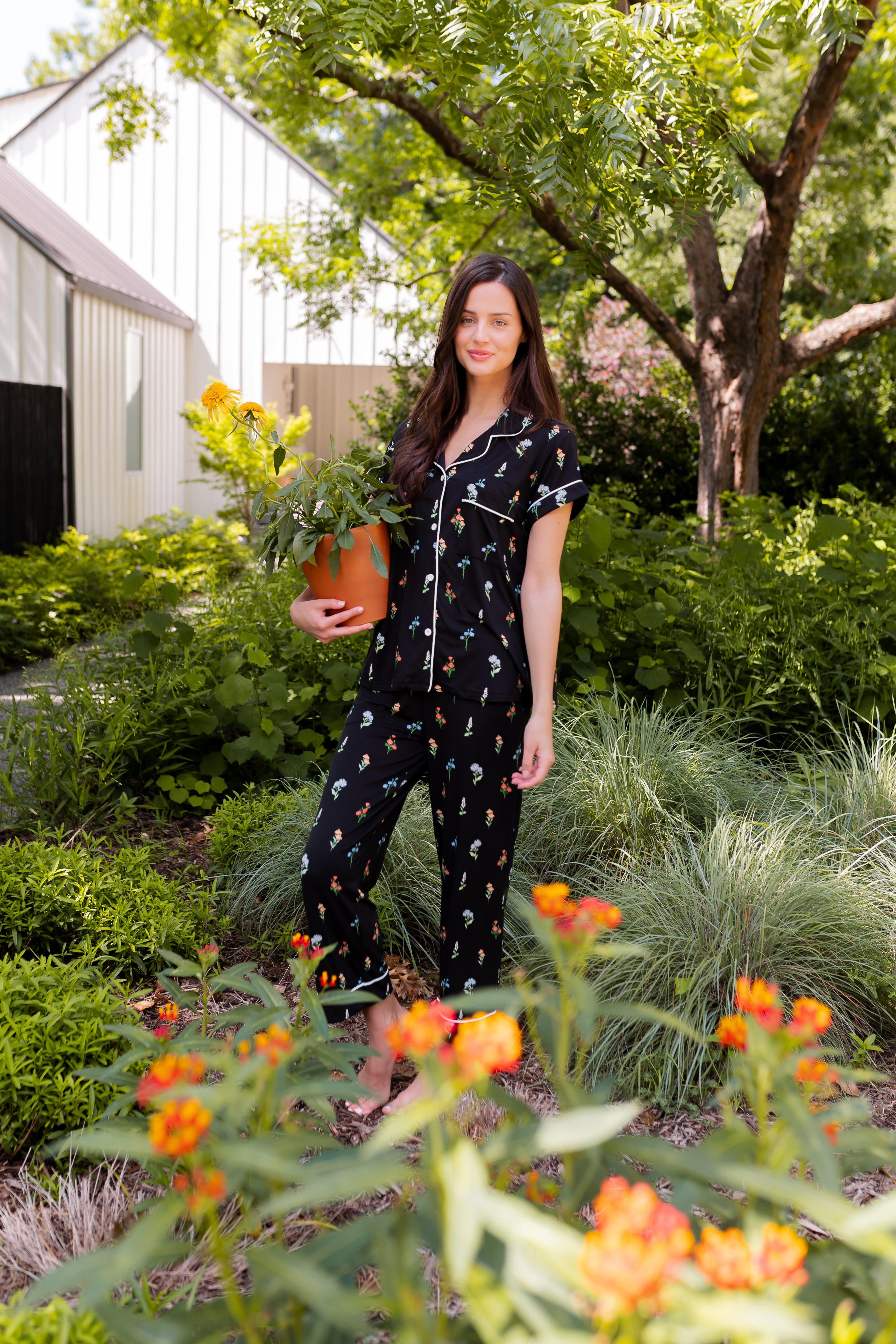 Model standing outdoors surrounded by trees holding a pot wearing Women's Short Sleeve Cropped Pajama Set in Midnight Wildflower  