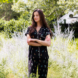 Model standing outdoors in bushes wearing Women's Short Sleeve Cropped Pajama Set in Midnight Wildflower print