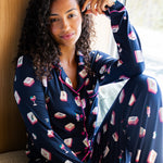 Woman wearing a navy pajama set with a mahjong pattern, sitting by a window.