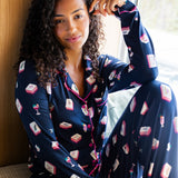 Woman wearing a navy pajama set with a mahjong pattern, sitting by a window.