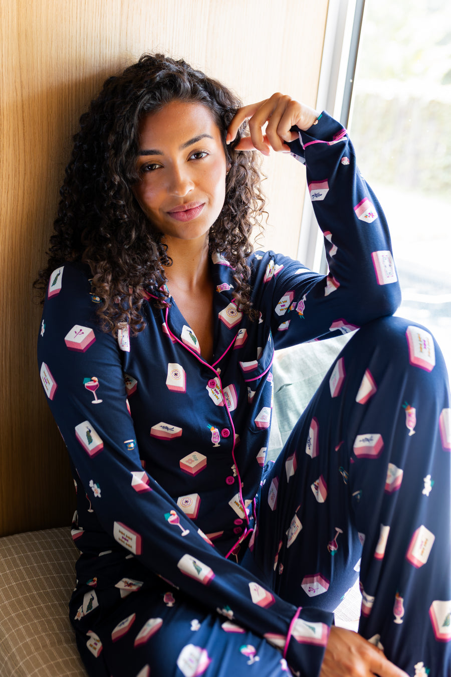 Woman wearing a navy pajama set with a mahjong pattern, sitting by a window.