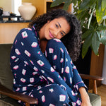 Woman in a navy blue pajama set with pink and white mahjong patterns sitting on a cushioned chair.