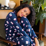 Woman in a navy blue pajama set with pink and white mahjong patterns sitting on a cushioned chair.