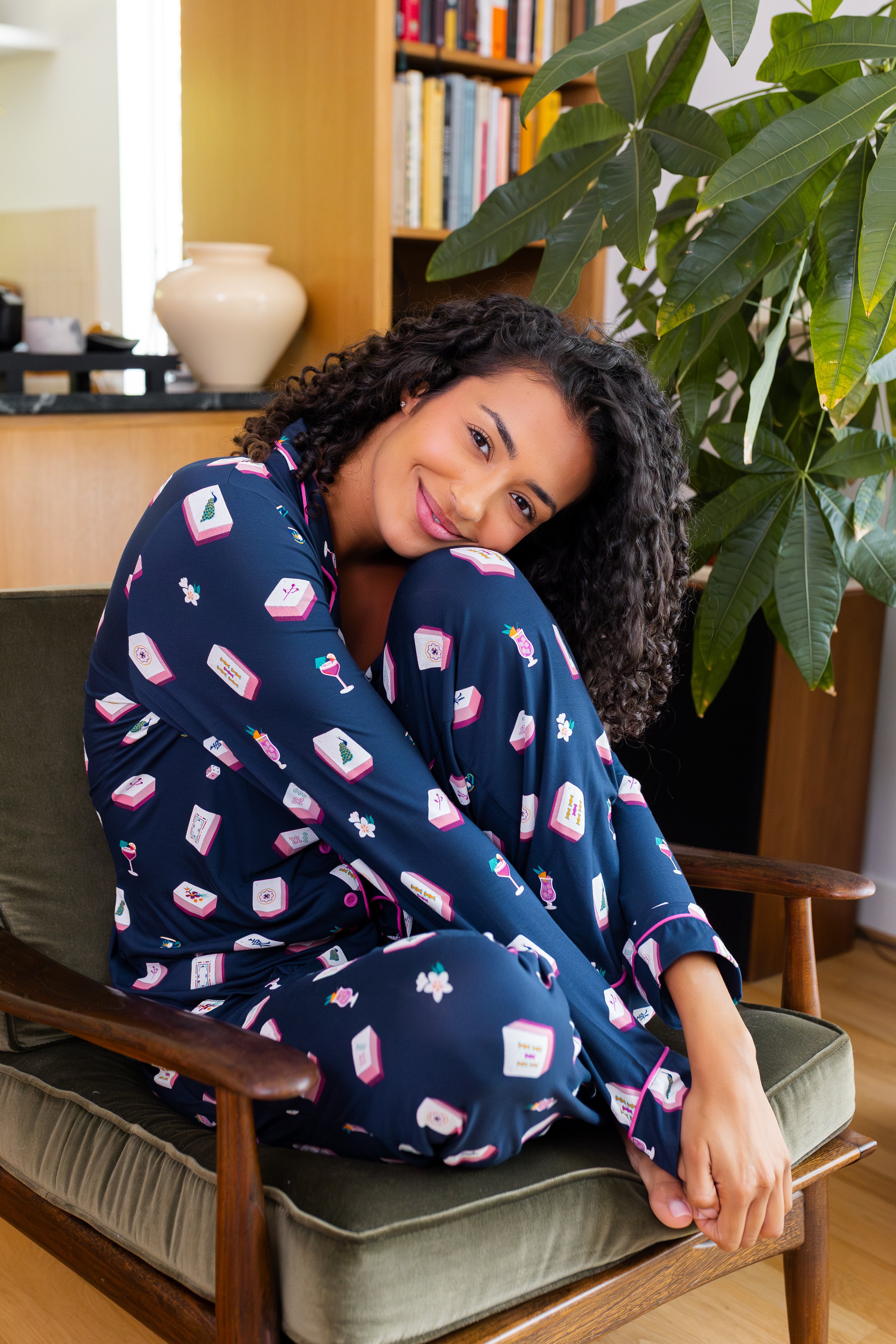Woman in a navy blue pajama set with pink and white mahjong patterns sitting on a cushioned chair.