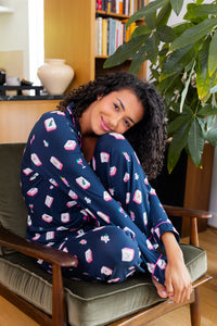 Woman in a navy blue pajama set with pink and white mahjong patterns sitting on a cushioned chair.
