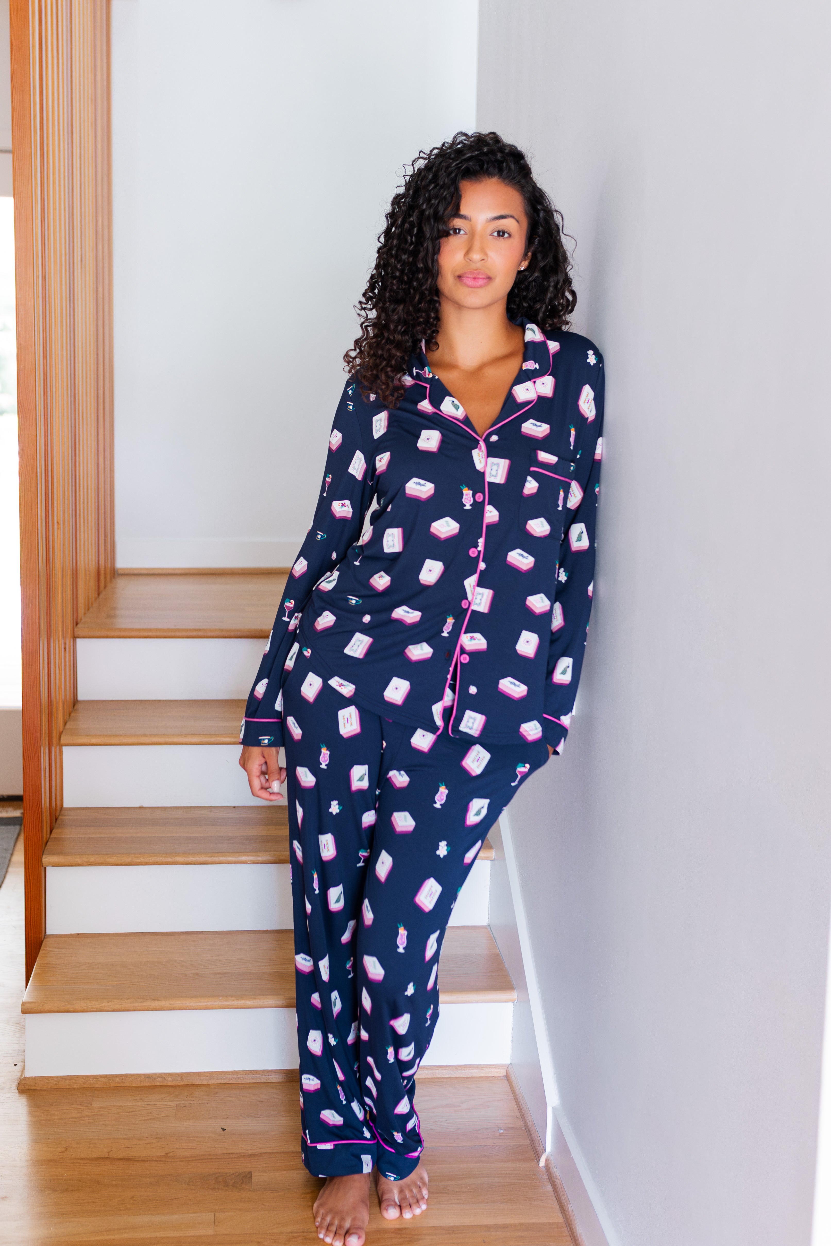 Woman wearing navy pajamas with pink mahjong pattern standing on a staircase.