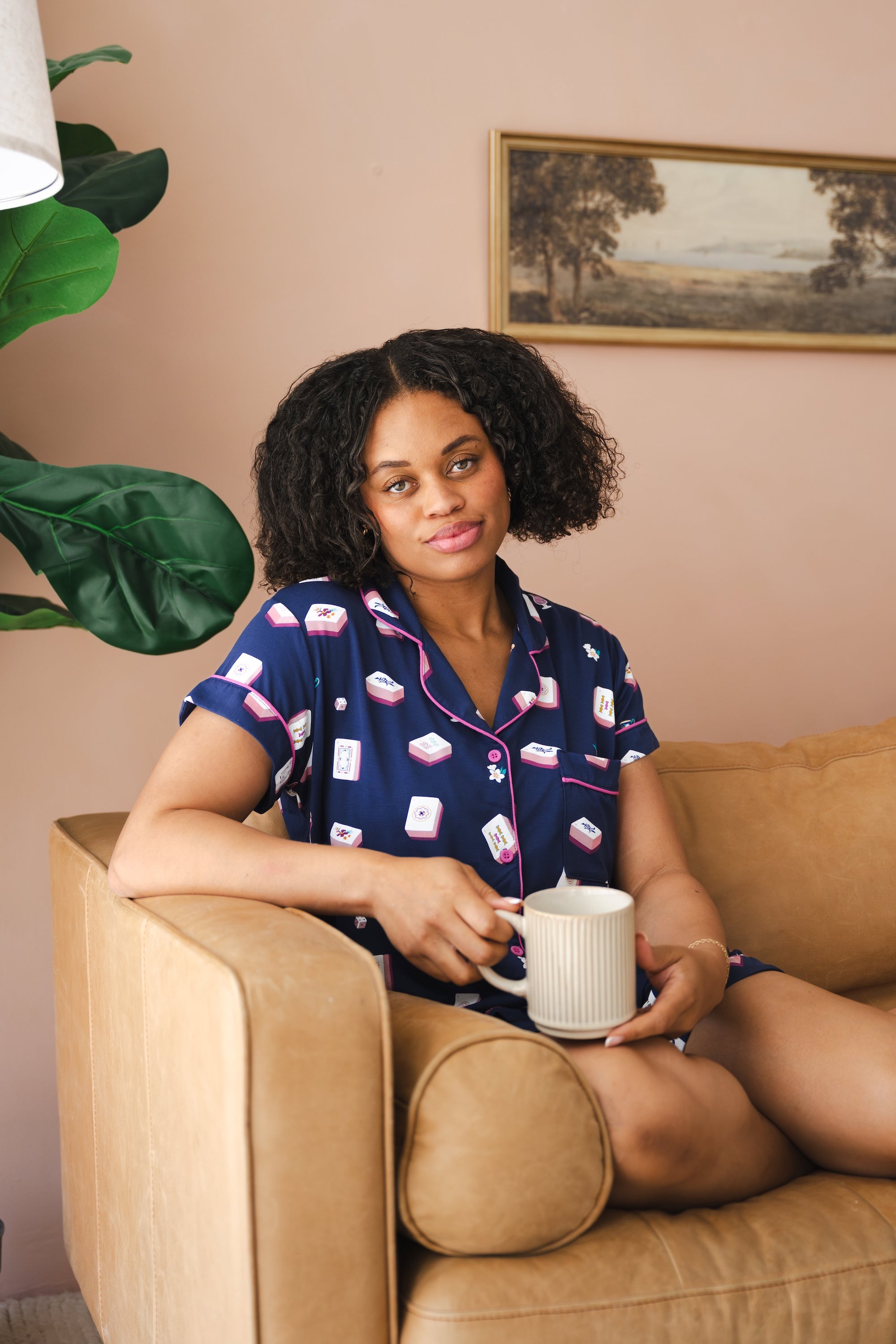 Woman holding a mug while sitting on a leather couch while modeling the Women's Short Sleeve Pajama Set in Navy Mahjong