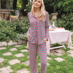 Woman standing in a grassy yard while modeling the Long Sleeve Women's Pajama Set in Patriotic Gingham with a picnic table behind her ::: Model is 5'9" wearing size XS ///