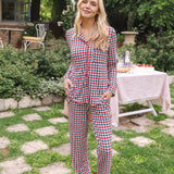 Woman standing in a grassy yard while modeling the Long Sleeve Women's Pajama Set in Patriotic Gingham with a picnic table behind her ::: Model is 5'9" wearing size XS ///