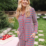 Woman standing next to a picnic table with a cake while modeling the Long Sleeved Women's Pajama Set in Patriotic Gingham

